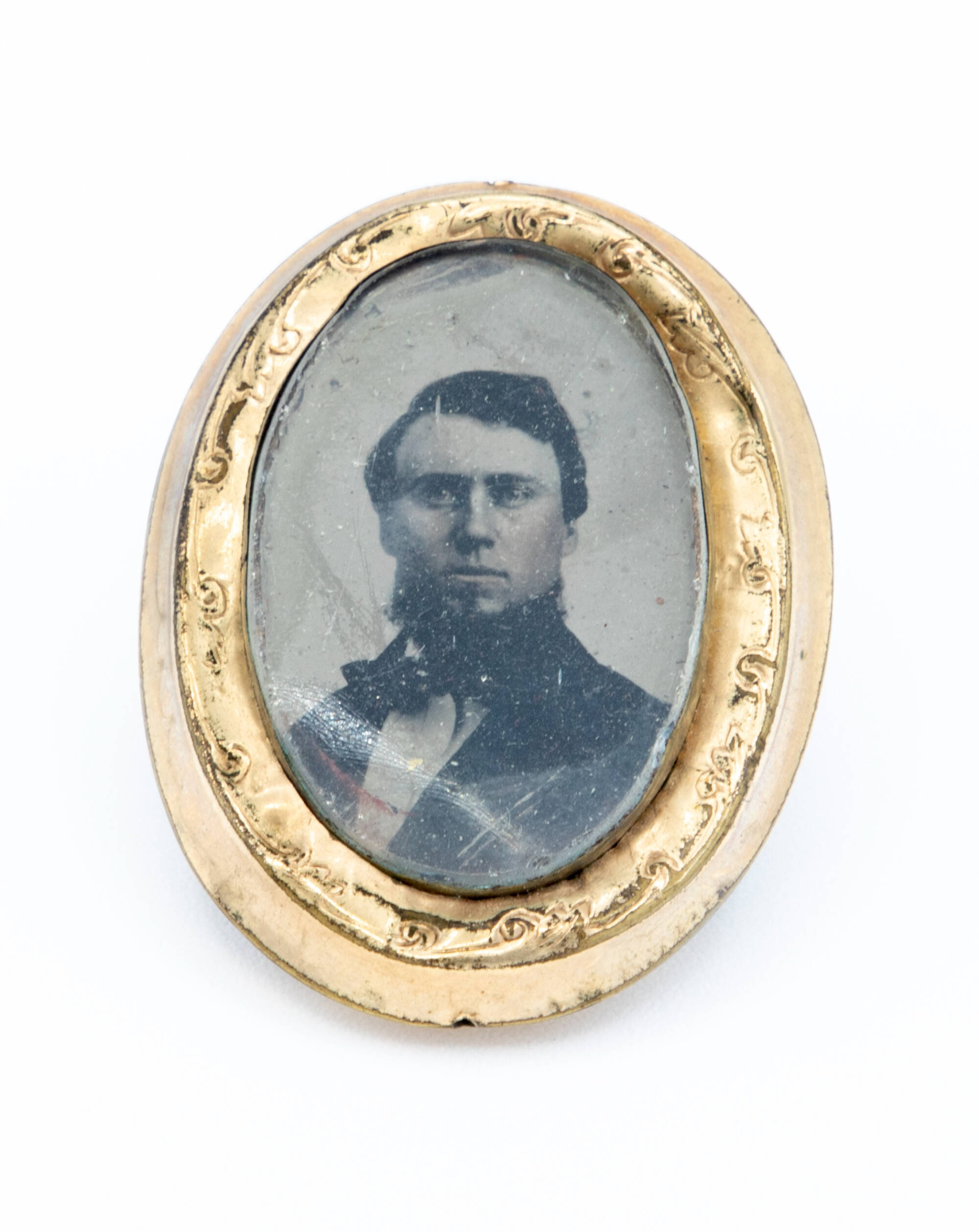 Black and white tintype photograph of a man inside of a gold frame pin.